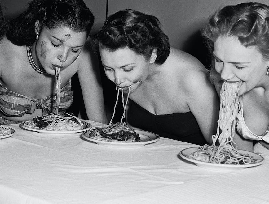 eating fun rivalry women head and shoulders portrait caucasian ethnicity dinner plate competitor flower arrangement spaghetti tablecloth american eating contest swimwear five people new york city table human person food meal dish