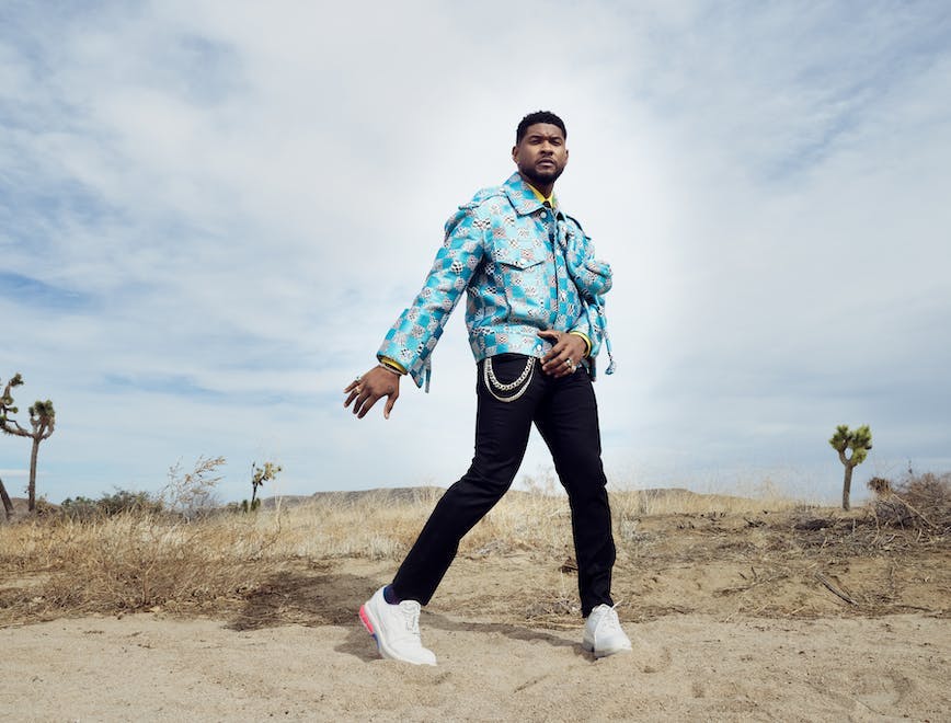 Usher indossa giacca di seta motivo Damier Distorted, camicia e pantaloni, cravatta di seta e scarpe "LV Fusion Derby", LOUIS VUITTON; orecchini e anelli con diamanti, JACQUIE AICHE; ear cuff, REPOSSI; anello, HOORSENBUHS; bracciale e anello, Usher's own. 
